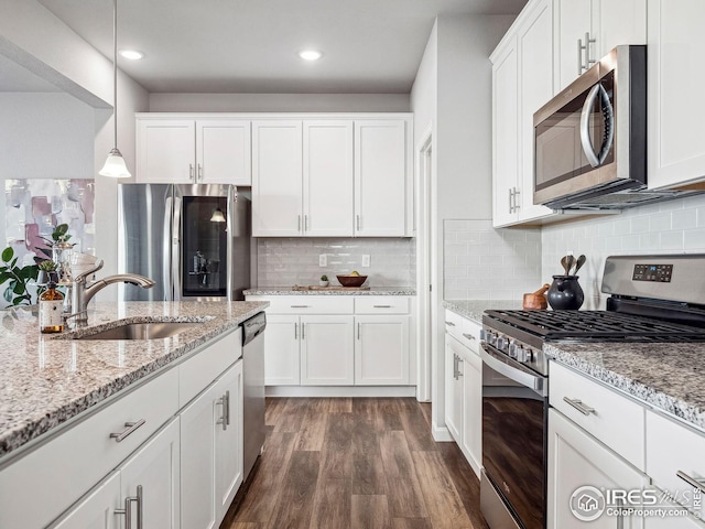 kitchen with appliances with stainless steel finishes, white cabinets, sink, pendant lighting, and dark hardwood / wood-style floors