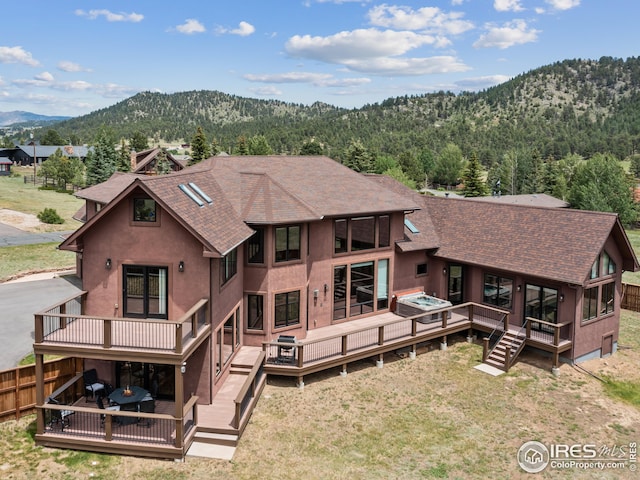 rear view of property featuring a forest view, fence, a deck with mountain view, and a shingled roof