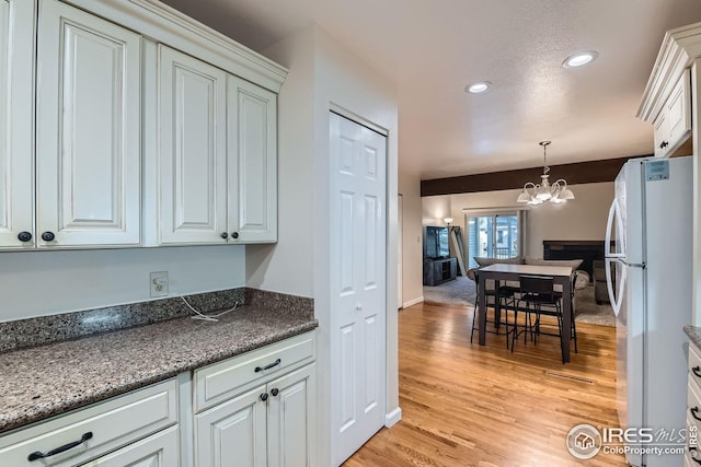 kitchen featuring light hardwood / wood-style flooring, hanging light fixtures, white refrigerator, white cabinets, and a notable chandelier