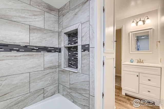 bathroom featuring wood-type flooring, a tile shower, and vanity