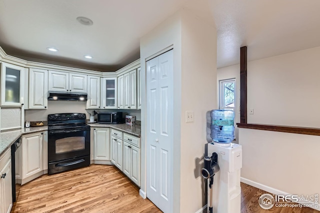 kitchen with black / electric stove, light hardwood / wood-style flooring, dark stone counters, and white cabinets