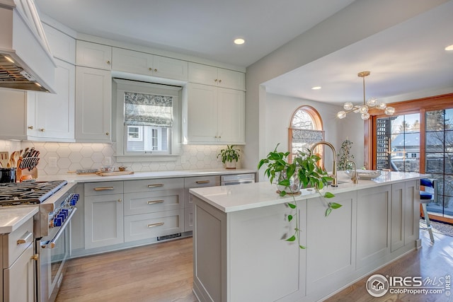 kitchen with pendant lighting, high end range, plenty of natural light, premium range hood, and a kitchen island with sink