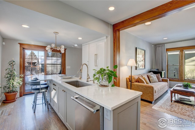 kitchen featuring a kitchen island with sink, stainless steel dishwasher, sink, decorative light fixtures, and light stone counters