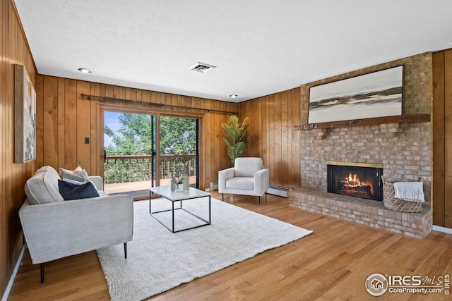 living room featuring hardwood / wood-style floors, a textured ceiling, a baseboard heating unit, a fireplace, and wood walls