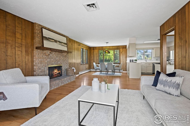 living room featuring a fireplace, sink, light hardwood / wood-style flooring, and wooden walls