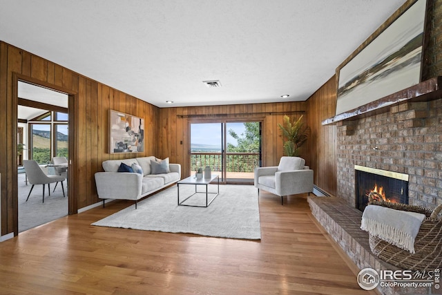 living room with baseboard heating, hardwood / wood-style floors, a textured ceiling, and a brick fireplace