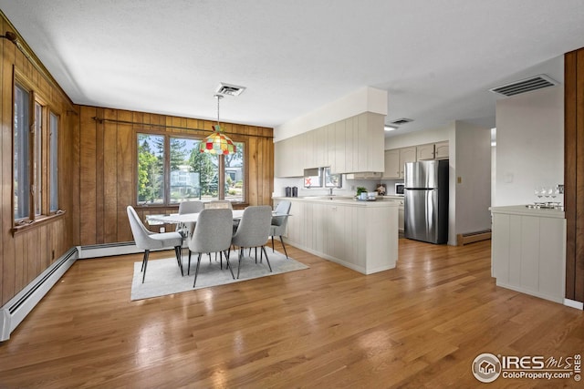 dining room with a baseboard radiator, light hardwood / wood-style flooring, and wood walls