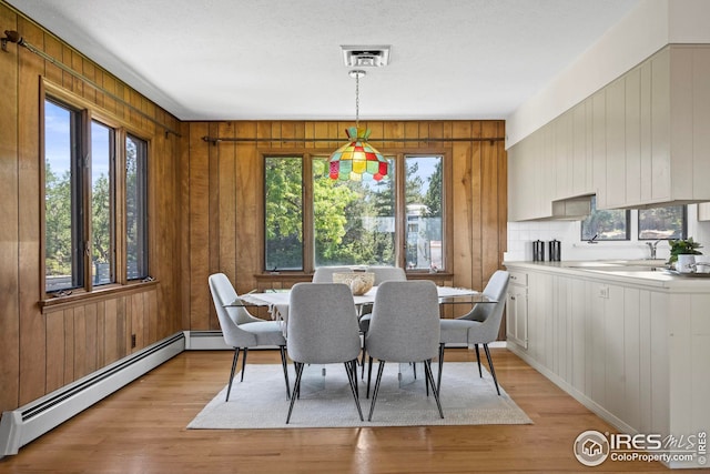 dining space featuring a baseboard radiator, a wealth of natural light, light hardwood / wood-style flooring, and wood walls