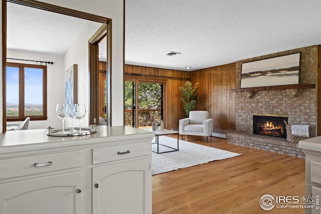 living room featuring a baseboard radiator, a textured ceiling, wooden walls, light hardwood / wood-style floors, and a brick fireplace