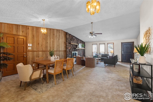 carpeted dining area featuring a stone fireplace, a textured ceiling, wooden walls, ceiling fan with notable chandelier, and lofted ceiling