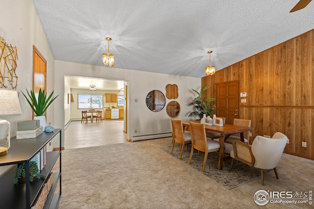 carpeted dining space featuring a chandelier, wooden walls, baseboard heating, and a textured ceiling