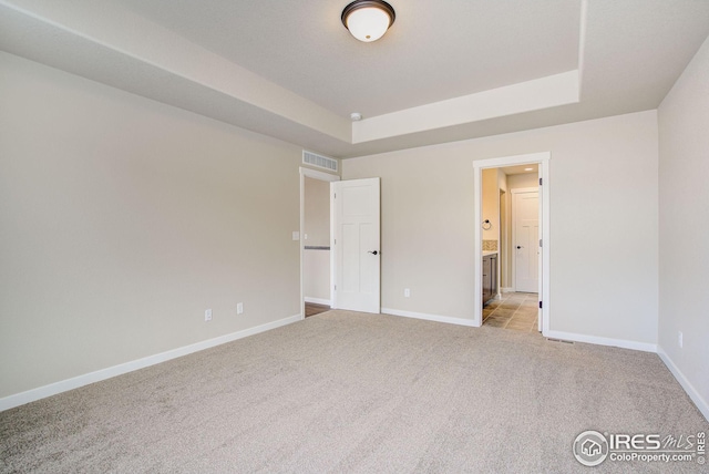 unfurnished bedroom featuring a tray ceiling, baseboards, visible vents, and light carpet