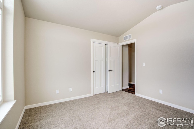 unfurnished bedroom with carpet floors, visible vents, baseboards, and vaulted ceiling