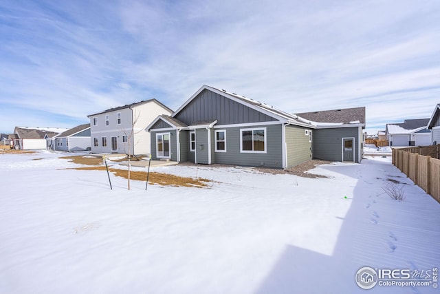 snow covered property with board and batten siding and fence