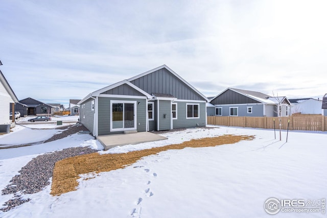 snow covered rear of property featuring fence and board and batten siding