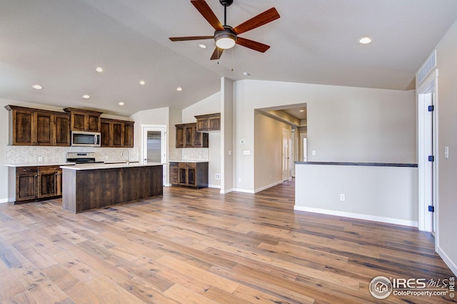 kitchen featuring light wood-type flooring, an island with sink, open floor plan, stainless steel appliances, and dark brown cabinetry