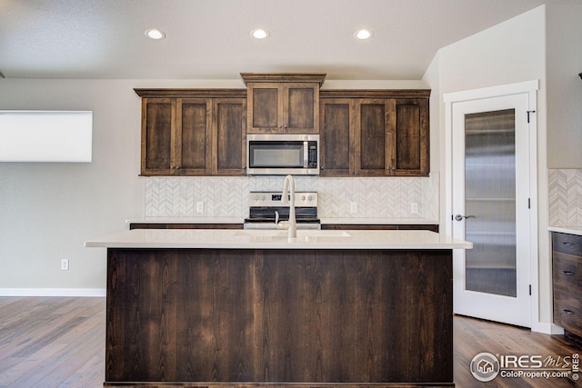 kitchen with a center island with sink, a sink, stainless steel appliances, light countertops, and dark brown cabinets