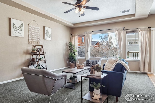 carpeted living room with a textured ceiling, a raised ceiling, and ceiling fan