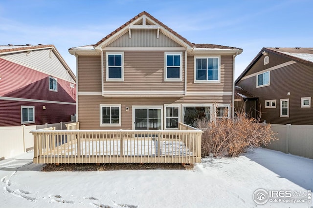 snow covered back of property with a wooden deck