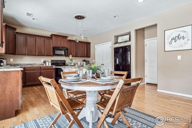 kitchen featuring a textured ceiling, light wood-type flooring, hanging light fixtures, and black appliances