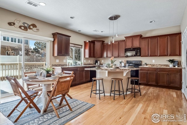 kitchen with a kitchen island, a kitchen breakfast bar, hanging light fixtures, black appliances, and light wood-type flooring