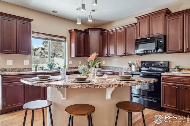 kitchen featuring light stone countertops, a center island, a breakfast bar area, and black appliances