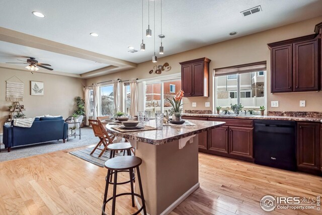 kitchen featuring a center island, hanging light fixtures, light hardwood / wood-style flooring, a kitchen breakfast bar, and black dishwasher