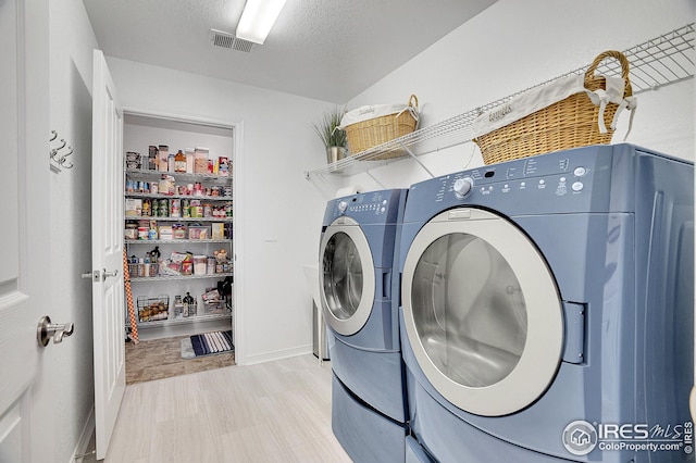 washroom with washer and clothes dryer, light hardwood / wood-style floors, and a textured ceiling