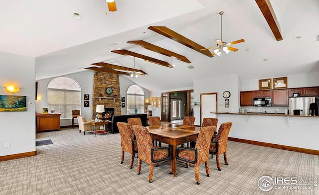 dining room featuring ceiling fan, high vaulted ceiling, a fireplace, light colored carpet, and beamed ceiling