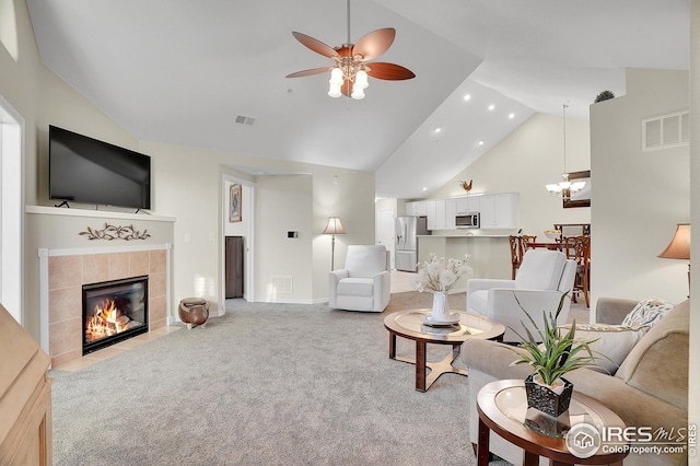 carpeted living room with high vaulted ceiling, ceiling fan with notable chandelier, and a tile fireplace