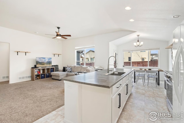 kitchen with sink, a kitchen island with sink, stainless steel range, white cabinets, and vaulted ceiling