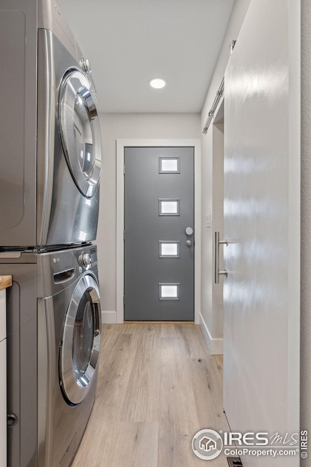 laundry area with stacked washing maching and dryer, a barn door, and light hardwood / wood-style floors