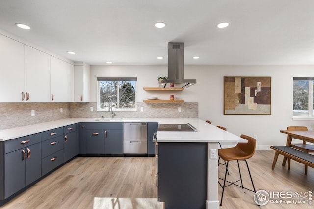 kitchen featuring sink, light hardwood / wood-style flooring, island exhaust hood, white cabinets, and a kitchen bar