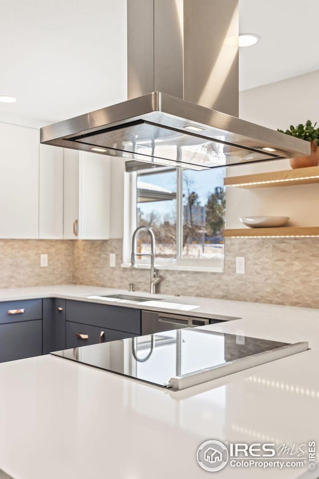 kitchen with blue cabinets, sink, island range hood, decorative backsplash, and white cabinets