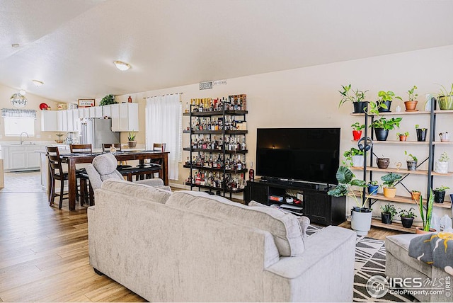 living room with sink, vaulted ceiling, and light wood-type flooring