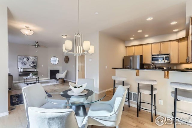 dining space with ceiling fan with notable chandelier and light hardwood / wood-style floors