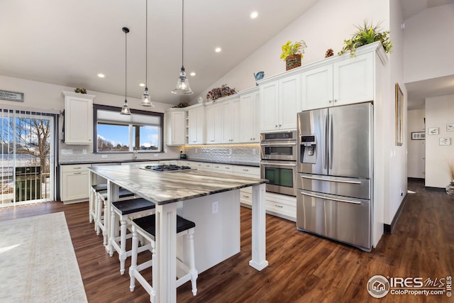 kitchen with stainless steel appliances, white cabinetry, light stone counters, and decorative light fixtures