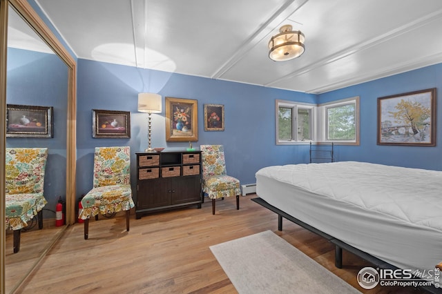 bedroom with beamed ceiling, a baseboard heating unit, and light wood-type flooring