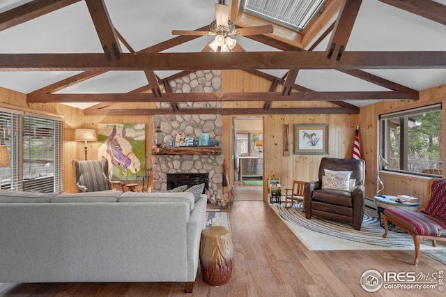 living room with ceiling fan, hardwood / wood-style floors, vaulted ceiling with beams, wooden walls, and a fireplace