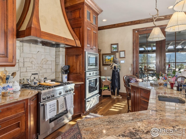 kitchen with sink, custom exhaust hood, hanging light fixtures, stainless steel appliances, and light stone countertops