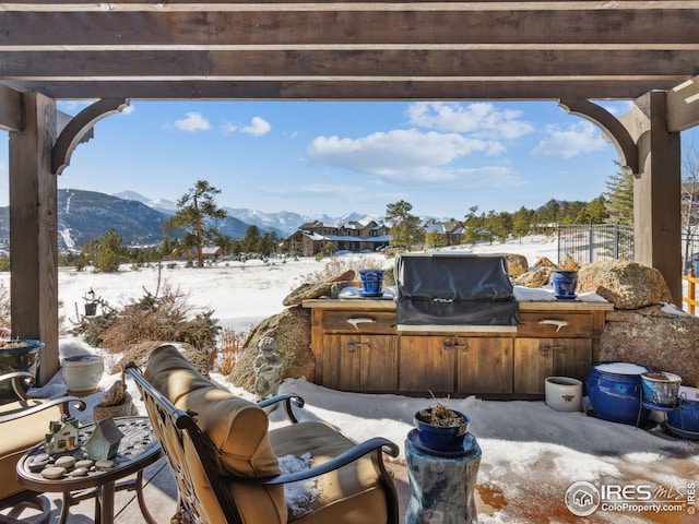 snow covered patio with a grill, a pergola, and a mountain view