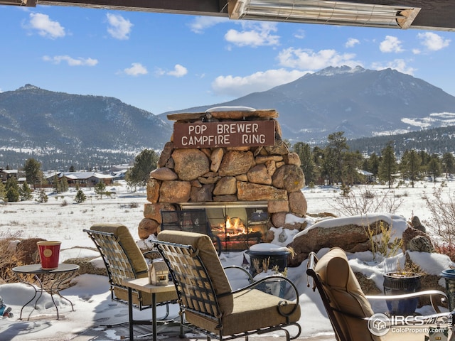 snow covered patio with a mountain view and an outdoor stone fireplace