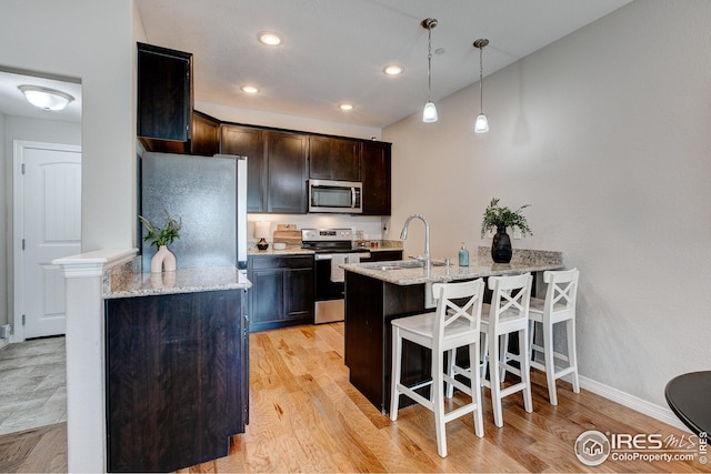 kitchen featuring stainless steel appliances, light stone countertops, hanging light fixtures, and light wood-type flooring