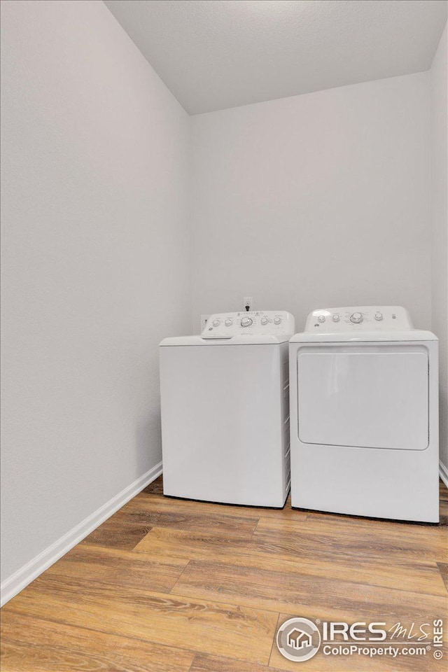 washroom featuring laundry area, washer and clothes dryer, baseboards, and wood finished floors