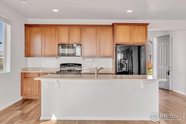 kitchen with black fridge with ice dispenser, light countertops, light wood-style flooring, stainless steel microwave, and range with gas cooktop