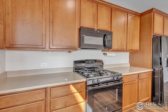 kitchen featuring light countertops, black appliances, and wood finished floors