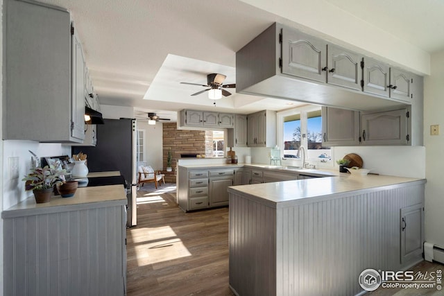 kitchen featuring a tray ceiling, light countertops, a sink, wood finished floors, and a peninsula