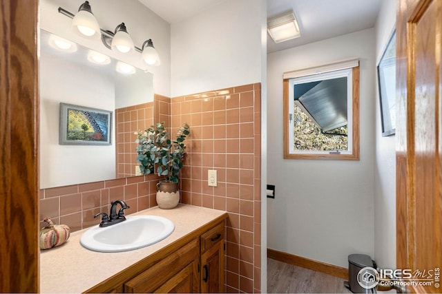 bathroom with wood finished floors, vanity, baseboards, a wealth of natural light, and tasteful backsplash