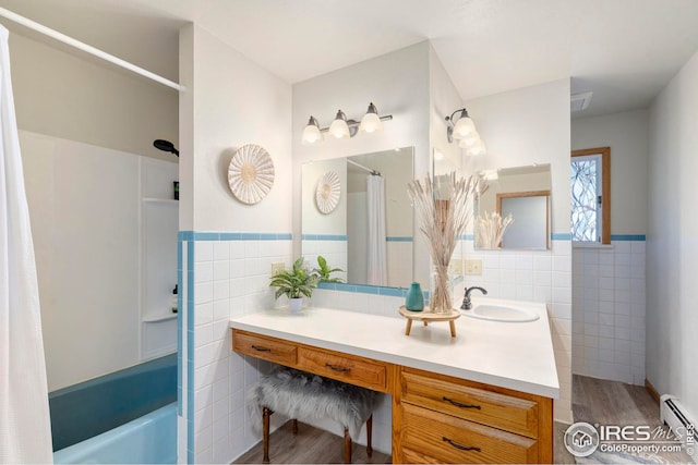 full bath with a wainscoted wall, wood finished floors, vanity, a baseboard heating unit, and tile walls