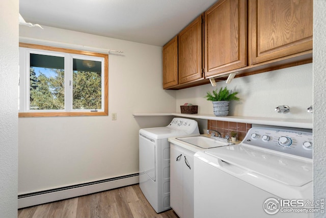 washroom featuring light wood-style flooring, a baseboard heating unit, a sink, cabinet space, and washer and clothes dryer